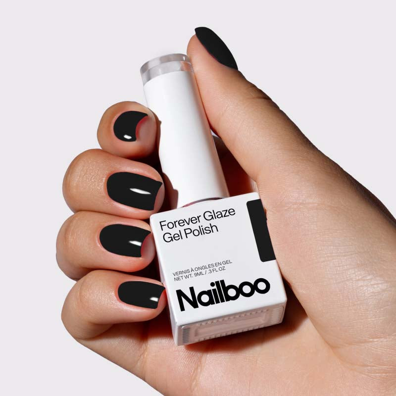 Hand with black manicured nails holding Nailboo Forever Glaze Gel Polish bottle.